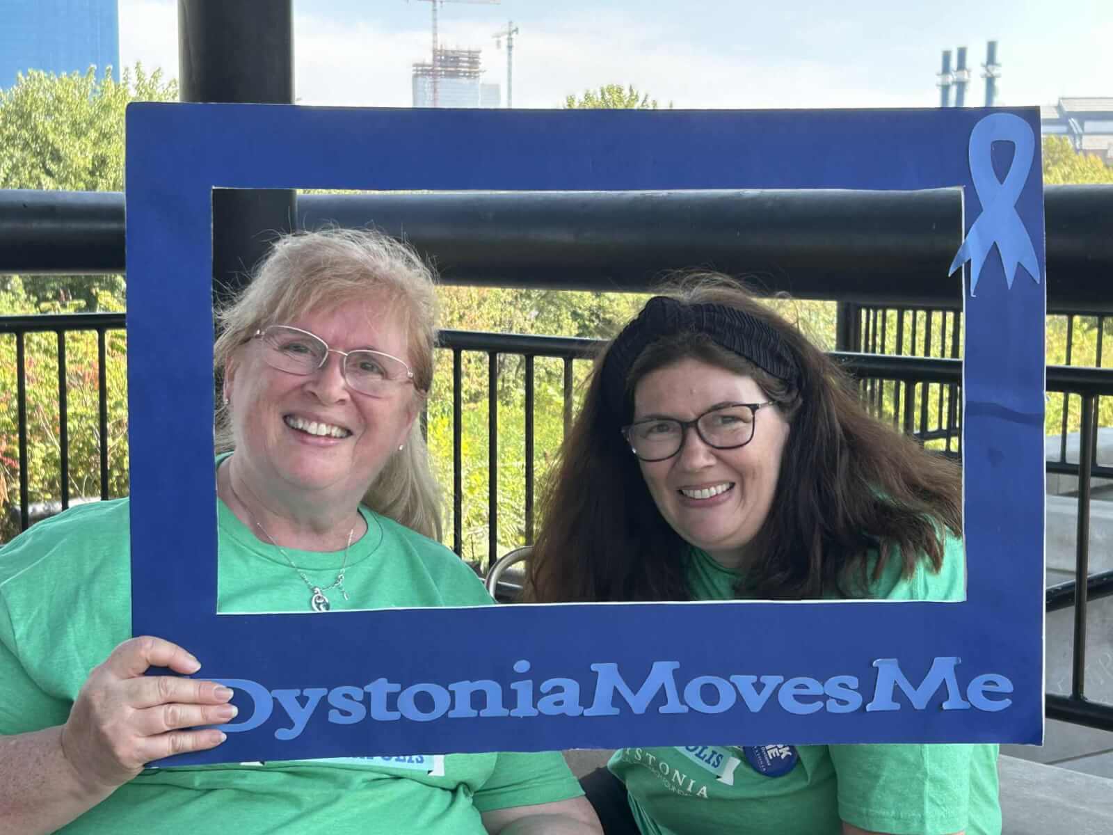 Two people holding a proper photo frame that says "Dystonia Moves Me".
