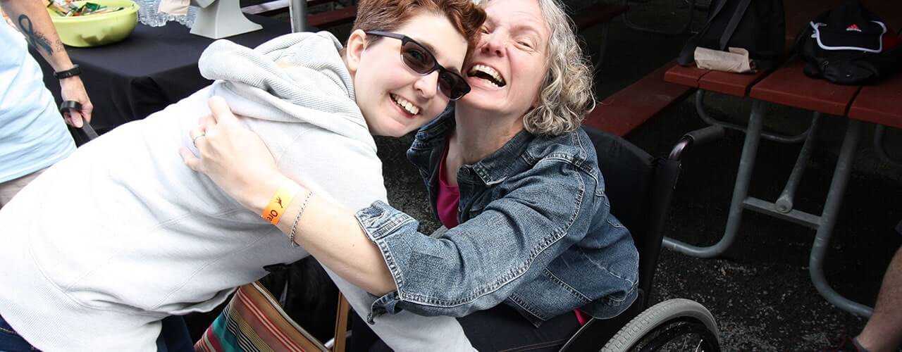 Two people hugging, one person standing and another in a wheelchair.