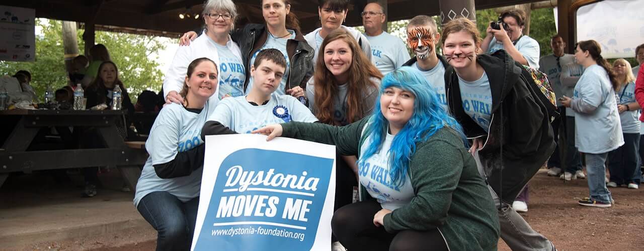 Group posing outside by a sign that reads "Dystonia Moves Me".